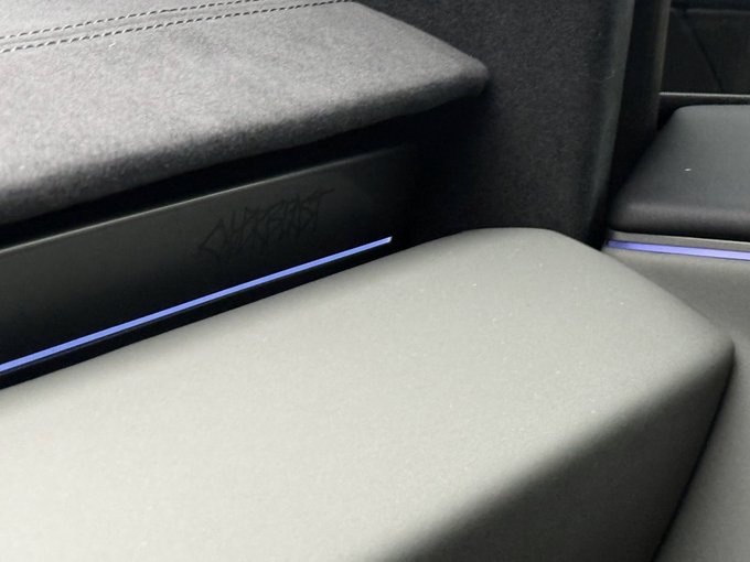 A close-up view of a car's interior shows dark leather seats, a textured headliner, and a decorative etched panel with purple ambient lighting.