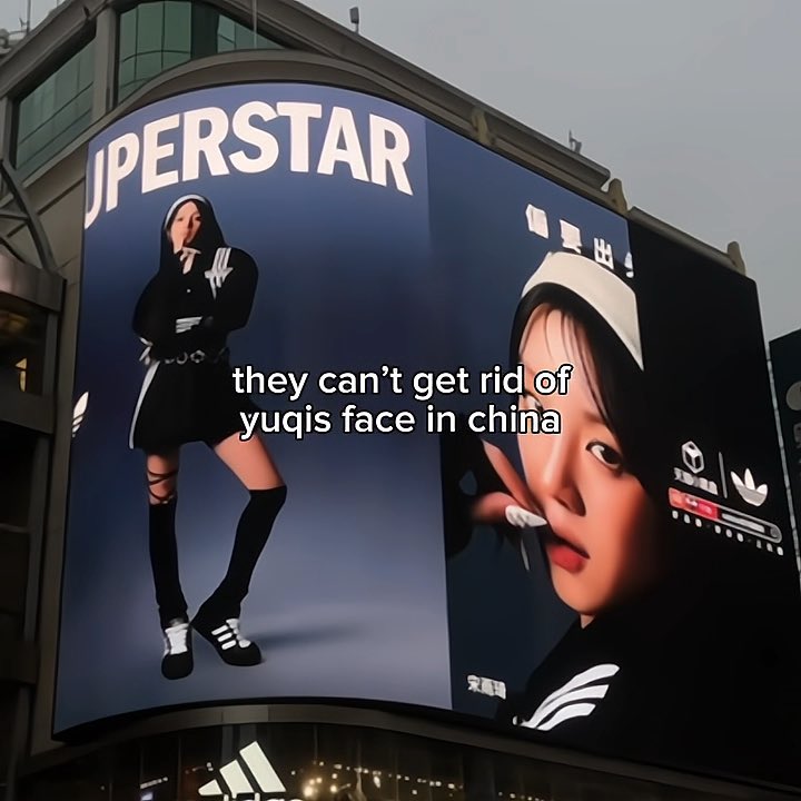 A large billboard advertisement displaying the word 'SUPERSTAR' alongside an Adidas Originals logo and images of a woman in sporty attire, with overlaid text reading 'they can't get rid of yuqis face in china'.
