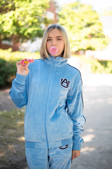 A picture of a woman wearing an Auburn tracksuit, blowing a bubble, and holding chewing gum.