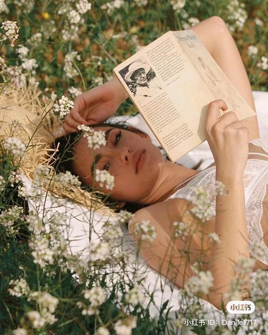 A woman lies in a field of white wildflowers reading a vintage book, with a Xiaohongshu watermark "小红书 ID: Danile1717" in the bottom corner.
