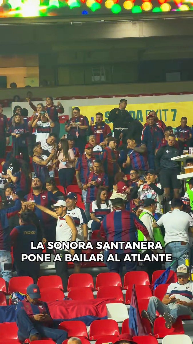 Atlante fans gather in the stadium stands, with a banner reading "SÚPER SORTEO EXIT 7" visible behind them and overlay text announcing "LA SONORA SANTANERA PONE A BAILAR AL ATLANTE," capturing the lively pre-halftime atmosphere during the Potros vs. Rayados match.