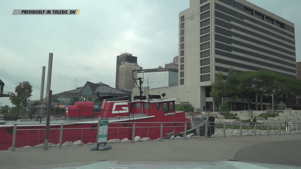 A red tugboat named "SUPERIOR" is docked along a riverfront in Toledo, Ohio, with the Renaissance Hotel and other downtown buildings visible in the background under an overcast sky, while an on-screen graphic reads "PREVIOUSLY IN TOLEDO, OH." The image serves as an establishing shot for a segment of "On Patrol: Live," which covers an incident involving officers responding to a call about a naked man eating from a garbage receptacle in the area.