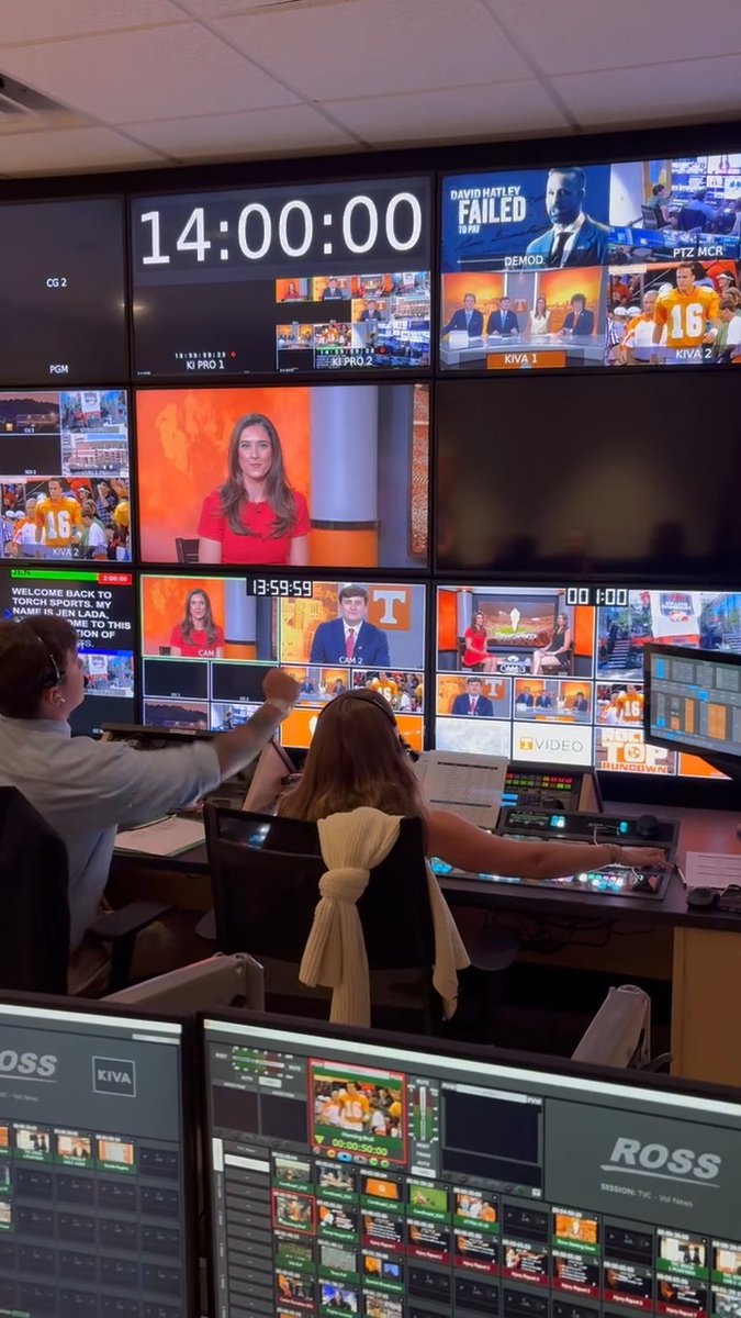 Television producers work in a control room filled with monitors displaying news broadcasts, a countdown timer reading '14:00:00,' and graphics for 'ROSS' software.