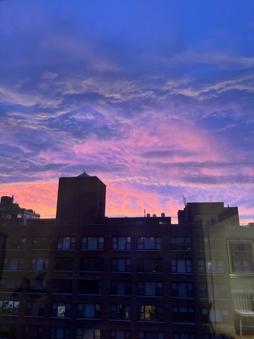 A vibrant purple and pink sunset sky over the silhouette of city buildings with water towers.