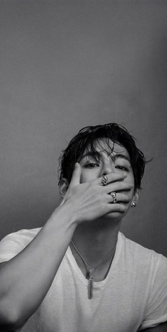 A black and white portrait of a young man with rings on his fingers covering his mouth.