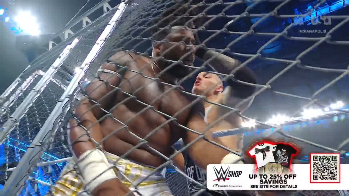The image captures intense action during a WWE Steel Cage Match in Indianapolis, showing two wrestlers locked in a physical confrontation against the cage wall under bright arena lights, directly illustrating Baron Corbin's fiery performance highlighted in the caption. The screen displays WWE Shop promotional text offering "UP TO 25% OFF SAVINGS" alongside a QR code.