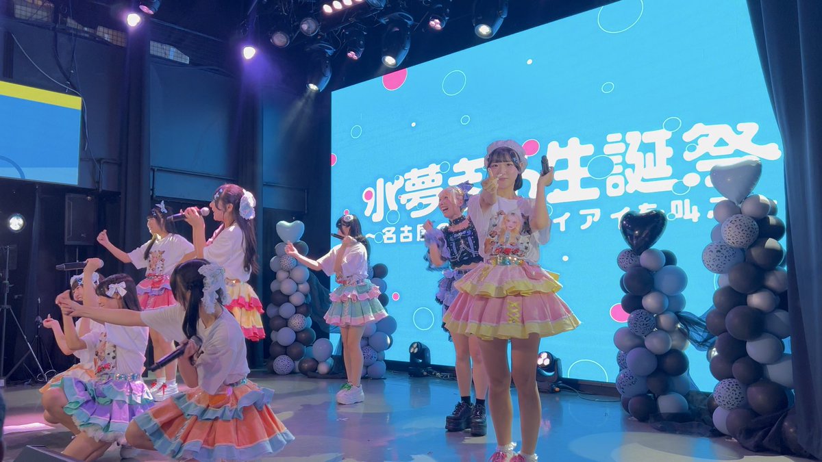 Members of the Japanese idol group 小夢見あかり (Komiyumi Akari) performing on stage in colorful frilly outfits at what appears to be a birthday live event.