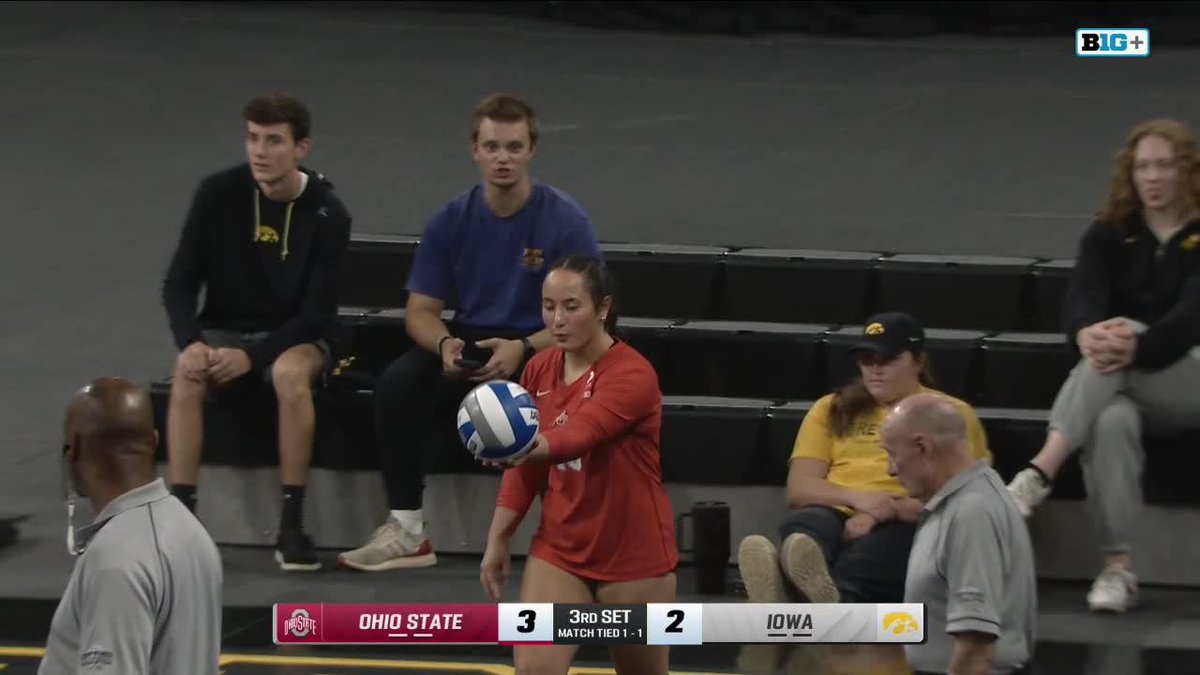 A broadcast screenshot from a B1G+ volleyball match between Ohio State (red) and Iowa (yellow), showing a player in red preparing to serve. Score overlay reads: 'OHIO STATE 3, IOWA 2 — 3RD SET, MATCH TIED 1-1'.