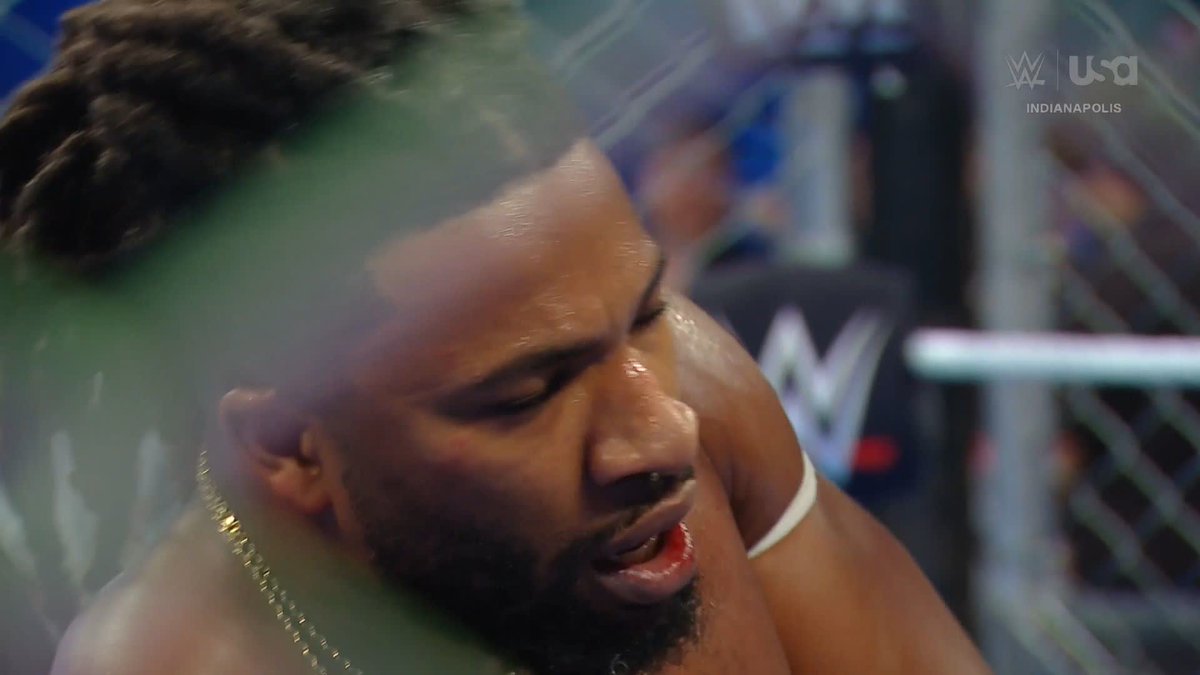 A close-up shot shows a male wrestler with dreadlocks and a beard inside a steel cage, with the 'WWE USA INDIANAPOLIS' logo visible in the corner.
