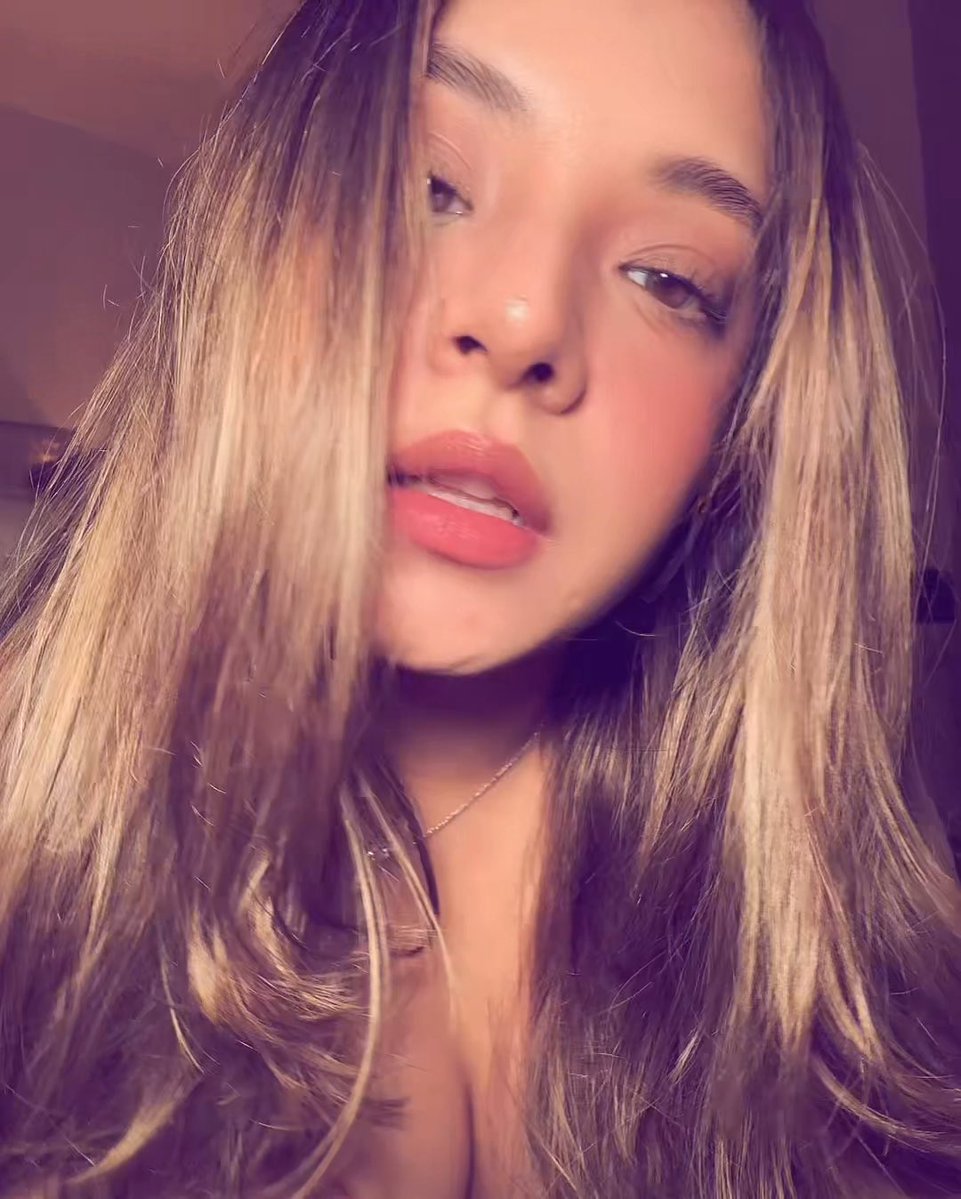 A close-up selfie of a young woman with blonde hair wearing coral lipstick.