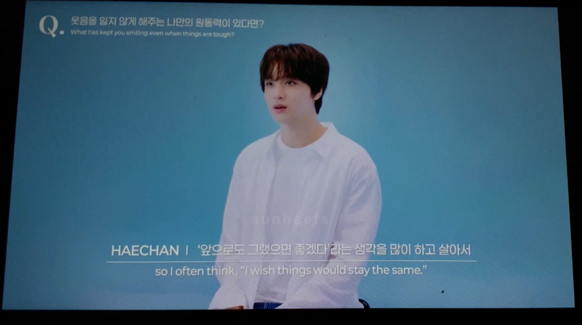 Haechan of NCT sits against a blue backdrop answering the question "What has kept you smiling even when things are tough?" with a subtitle reading "HAECHAN | so I often think, 'I wish things would stay the same,'" reflecting his words about drawing strength from the members and their shared memories.