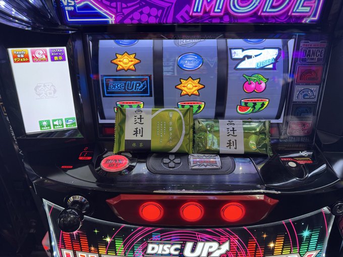 A "DISC UP2" pachinko machine with glowing red buttons and vibrant displays holds two packages of "辻利" (Tsujiri) green tea sweets, Japanese souvenirs gifted as mentioned in the post thanking ジャパン for a Kyoto souvenir, たき for a Hokkaido souvenir, and たまやん for drinks.