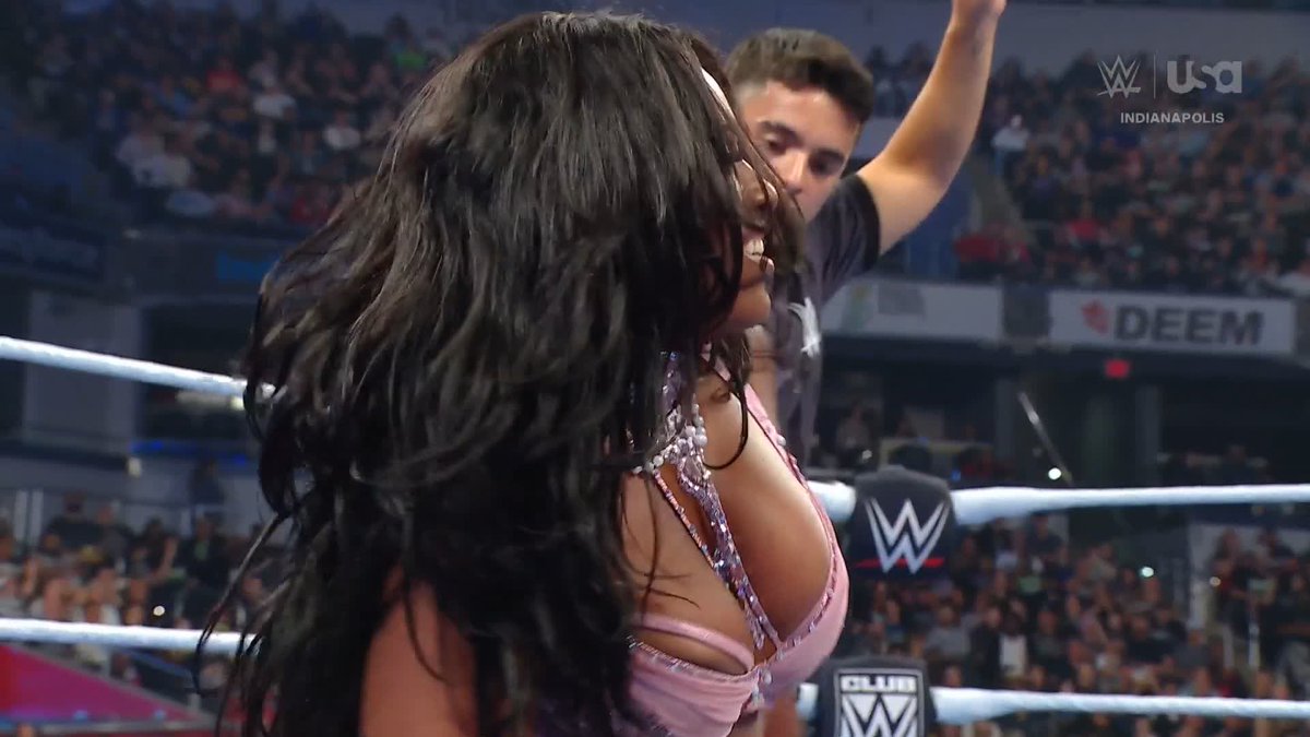 A WWE wrestler with long dark hair stands inside the ring at an event in Indianapolis, with the "USA" and "WWE" logos visible, while the accompanying post questions why Lash Legend receives more premium live event opportunities than Giulia despite the latter having more fan buzz and in-ring activity.