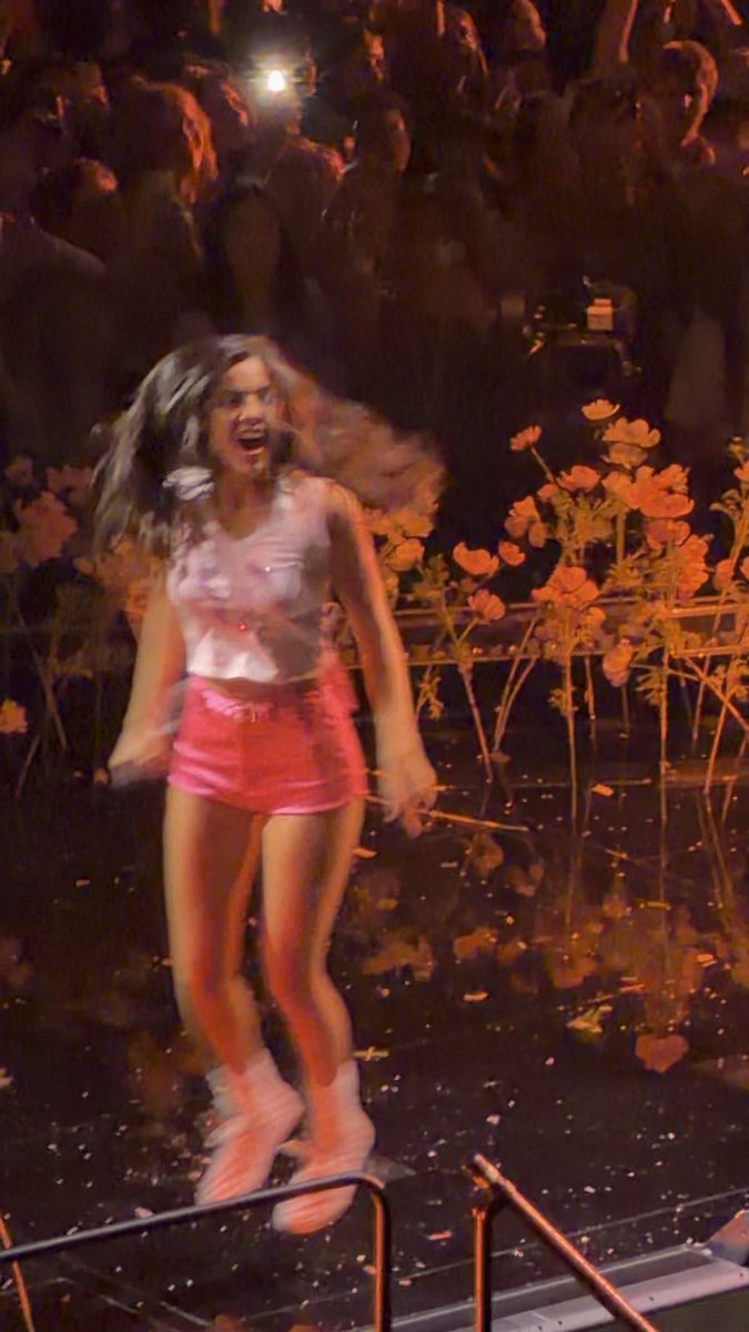 Olivia Rodrigo performs energetically on stage during opening night of "The Unraveled Tour" in Hartford, wearing a pink crop top, red shorts, and pink boots while singing "Bad Idea Right?" in front of an illuminated crowd.