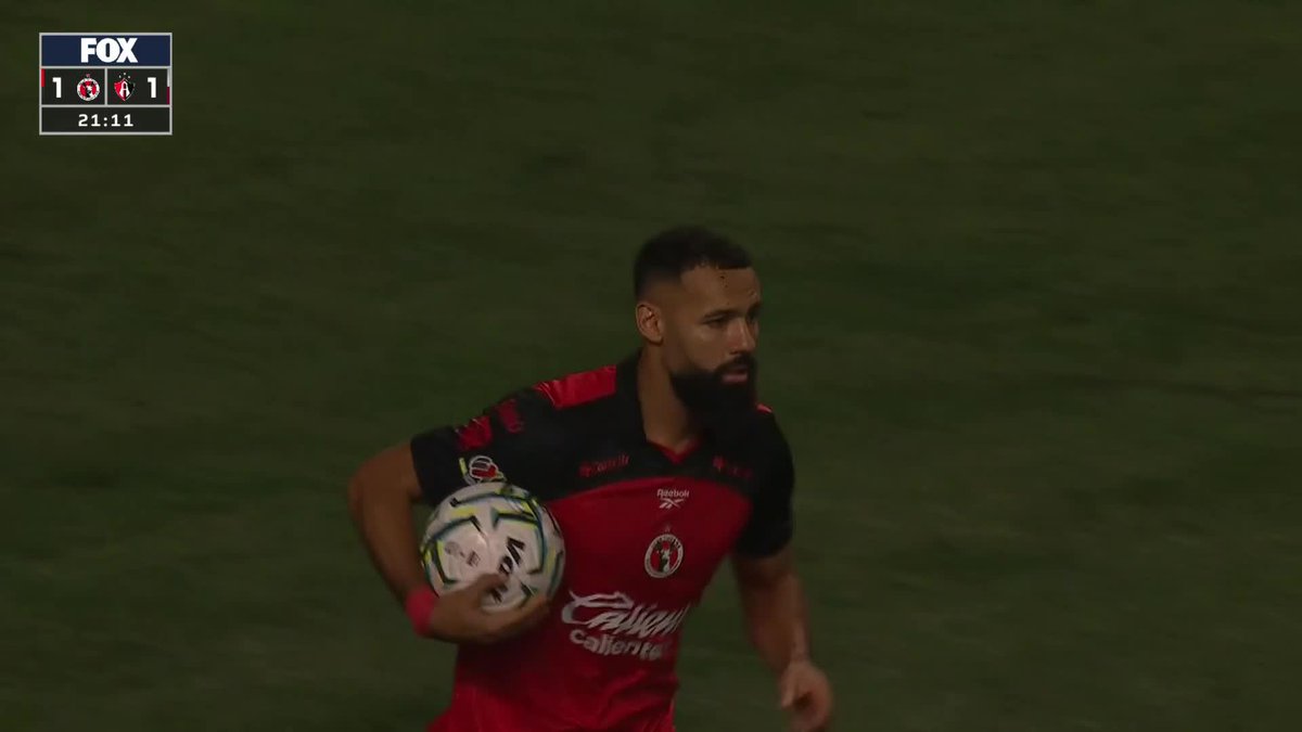 A Xolos player holds the match ball after scoring a penalty kick, with the FOX scoreboard showing a 1-1 tie at 21:11, tying the match for "La Jauría."