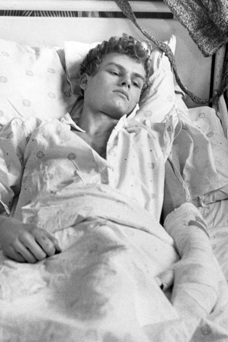 archeohistories's tweet photo. Wolfgang Engels was a 19-year-old East German border guard. He drove a Soviet-built armored vehicle through the Berlin Wall on April 25, 1963. Border guards shot him as he tried to exit the vehicle, causing the wounds seen in this photo taken at the Urban Hospital.... 

On April 17, 1963, a 19-year-old East German rammed an armored vehicle into the Berlin Wall. Wolfgang Engels was not a patrolling soldier, but a civilian auto mechanic trapped inside a stolen six-ton armored personnel carrier accelerating toward concrete and concertina wire. For twenty months, the German Democratic Republic had sealed its border with watchtowers, minefields, and shoot-to-kill orders. Dozens had already died attempting to swim border canals or leap from windows into Western fire nets. Engels knew that civilian cars crumpled against fortified obstacles, ending in prison or death. His only chance lay in raw steel momentum. Driving through darkened East Berlin streets, he steered the combat carrier directly toward the frontier, betting his life on a single catastrophic collision.

The audacious escape grew from profound ideological disillusionment. Born in Düsseldorf during the Second World War, Engels was brought to the Soviet zone as a boy by his mother, an ardent communist official in the ruling Socialist Unity Party. Despite his family’s elite status, Engels despised the censorship and pervasive surveillance of the Stasi. In August 1961, while serving as a driver in the National People's Army, he was deployed to the border when barbed wire was first strung across Berlin. Ordered to stand guard while workers bricked up streets and separated families, Engels was horrified to realize he was helping build a cage for his own people. That trauma haunted him, turning a private longing for freedom into an obsessive search for an escape route.

Working as a civilian mechanic at an army depot in 1963, Engels found the machine that could pierce the barrier: a six-wheeled Soviet BTR-152 armored personnel carrier. On the evening of April 17, while depot guards were distracted during dinner, Engels started the engine and drove past the gate, pretending to conduct a routine maintenance test. Driving through residential streets, he made a reckless stop, shouting to startled pedestrians: "Does anyone want to ride to the West?" Terrified that the offer was a lethal Stasi provocation, the civilians scattered in panic. Realizing he was entirely alone, Engels turned toward Treptow, aiming for the intersection of Elsenstraße and Heidelberger Straße, where the wall divided East Berlin from the Western district of Neukölln.

Approaching the frontier, Engels cut the headlights, dropped the steel armored view slits, and slammed the accelerator to the floor. Roaring down the asphalt in total darkness, the carrier crashed into the cinderblock barrier at full speed. The impact tore through the masonry, throwing Engels violently against the dashboard. But the wall did not crumble as planned. While the vehicle's armored snout punched into Western territory, the undercarriage became stranded on the shattered concrete foundation, its wheels spinning in midair while concertina wire tangled the axles. Trapped halfway between East and West, Engels kicked open the top hatch and scrambled onto the armored hood, directly into the crosshairs of a nearby watchtower.

#archaeohistories