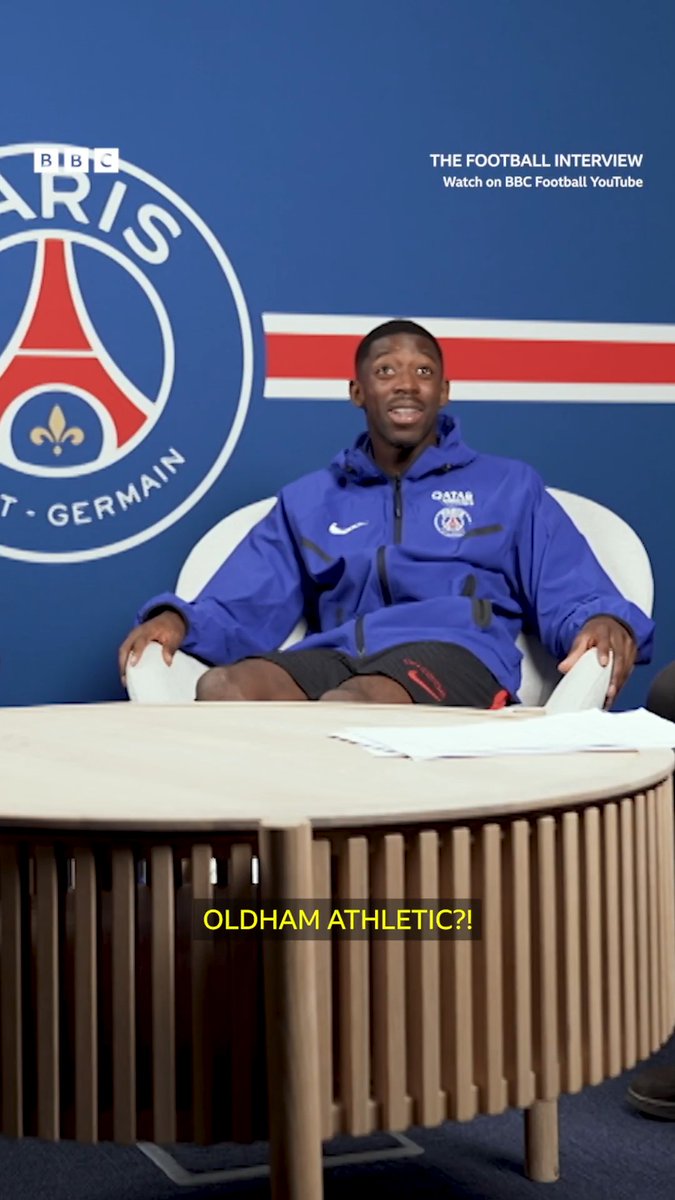 Ousmane Dembélé, wearing a Paris Saint-Germain training jacket, sits in a white chair during a BBC Football Interview with a Paris Saint-Germain branded backdrop, reacting with surprise as the caption reads "OLDHAM ATHLETIC?!" referencing his disbelief about the lower-league English club.