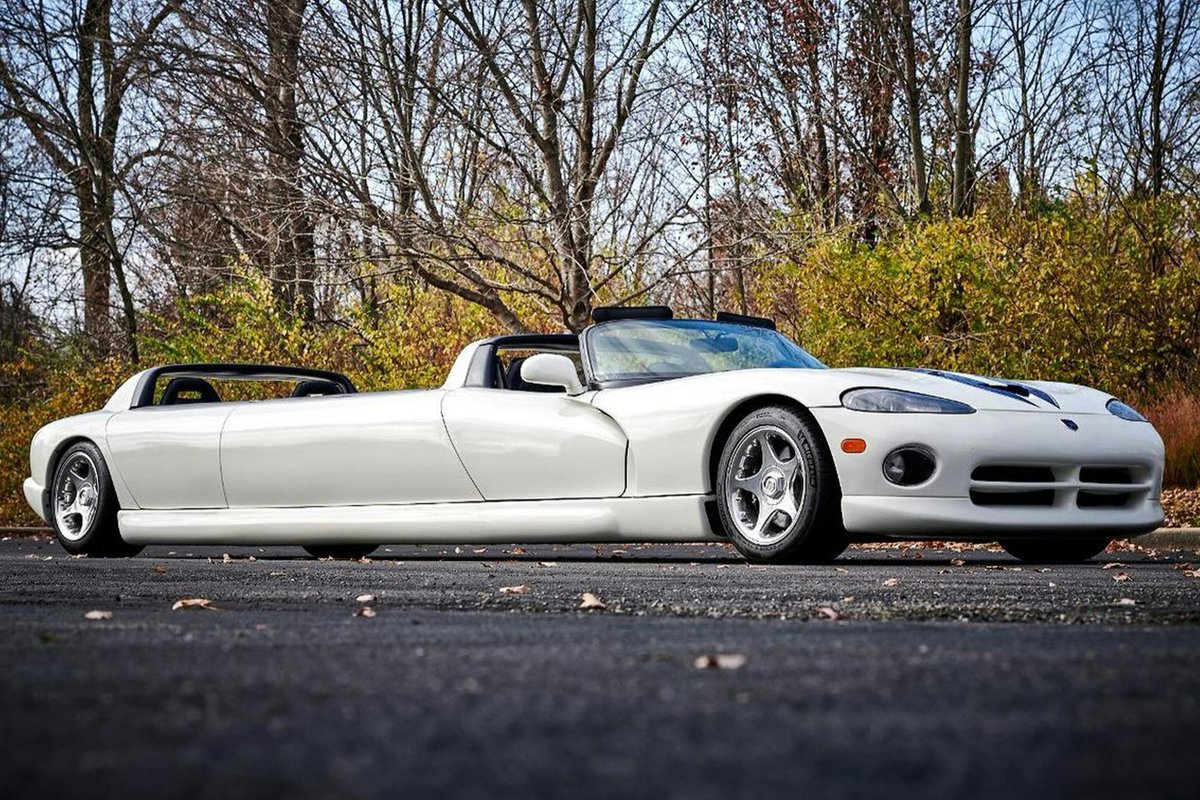 car_kobanashi's tweet photo. ダッジ バイパー RT/10 リムジン（1996 アメリカ）
1996年型「ダッジ バイパー RT/10」をベースに製作されたこのストレッチリムジンは、劇中車制作などで知られる米ラスベガスの「ユニーク・ムービー・カーズ」が手掛けた特装モデルである。大排気量アメリカンスポーツのシャシーを大胆に延長し、全長は25フィート（約7.6メートル）に達する。屋根のないオープン構造を保ちつつ、前席後方のロールバー造形を後端シートの後ろにも増設した独特のスタイリングを持つ。

車体中央の延長部分には対面式のロングベンチシートを新設。前席2名、車体後端の独立バケットシート2名と合わせ、販売時には最大12名乗車が可能と宣伝された。ホワイトのボディにブルーのストライプという伝統のカラーリングを纏い、荷室には大音量オーディオシステムを駆動するパワーアンプやオプティマ製バッテリーが搭載されている。

注目すべき変更点は動力部に存在する。本来の8.0リッターV型10気筒と6速MTは降ろされ、クライスラー製360立方インチ（約5.9リッター）「マグナム」V型8気筒エンジンへと換装。さらに変速機も純正設定のないオートマチック（AT）へと変更されているが、運転席にはダミーの6速MT用シフトノブが残され、視覚的な雰囲気を演出している。

この換装は、過激なV10よりも低速巡航やパレード運行における扱いやすさと熱管理を優先した現実的な選択といえる。獰猛な本格スポーツと華美なリムジン文化が融合した、極めて特異なアメリカンカスタムらしい車である。#車小噺
