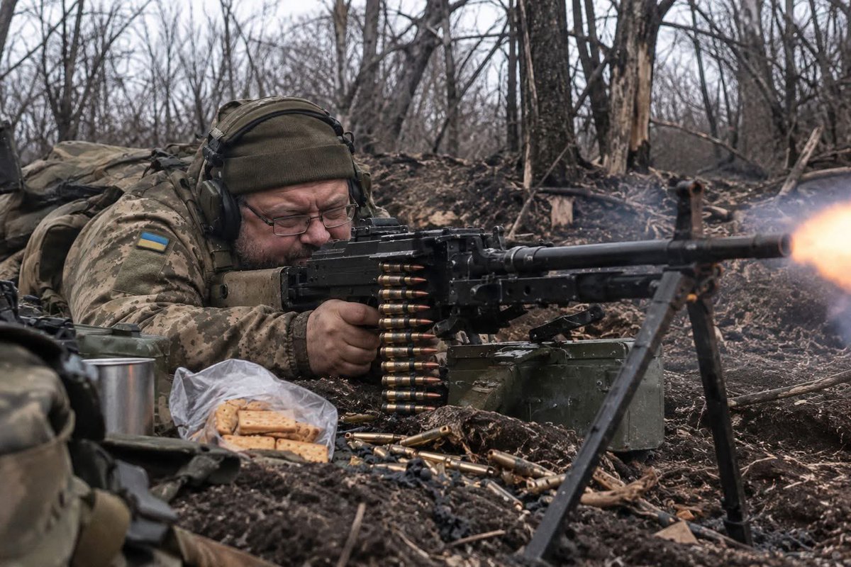 volodarskijo's tweet photo. Якщо вам здається, що мамині синочки не створені для війни, - ви просто не знали Вітю.

Років сорок п’ять. Окуляри. Живіт такий добрий, домашній. Обличчя людини, яка може пів години вибирати сметану в АТБ, бо "ця щось подозрітєльно дешева". 

Тихий. Скромний.  Ніхто б не подумав, шо ця людина за годину може лежати посеред розбитої посадки й методично виписувати з кулемета такі рахунки, які вже ніяка бухгалтерія не закриє.

Вітя дуже любив маму. Не в тому сенсі, що на восьме березня дзвонив. Ні.

Вітя був із мамою на зв’язку так, наче вона командувала окремим оперативним угрупованням військ "Синочок".

- Мам, я поїв. Гречка була. Нє, не холодна. Шапку вдягнув.

І сидить 45-річний кулеметник у корчі навколо БК, броніки, автомати, банка тушонки (з датою виробництва ще при Порошенко) і двадцять хвилин пояснює мамі чому в нього трохи кашель. 

А потім уважно слухає: 

- Вітя ти дивись там. Не застуди горло. 

І найсмішніше - Вітя слухав. Бо мама для нього була вищим командуванням.

Командир міг сказати: тримати позицію. Вітя кивав.

Мама казала: - Ти там бережи себе.

І це вже був реальний наказ.

При цьому, кулеметником Вітя був страшним. Хто не знає: кулеметник в піхоті - це така професія, де роботодавець одразу натякає, що кар’єрний рост може бути дуже коротким. 

Бо коли починається штурм - всі дуже швидко шукають, звідки насипає кулемет. І коли знаходять - туди летить усе. 

Автомати. Гранати. Міномет. Арта. Прокльони. Бо кулемет треба заткнути першим. 

А Вітя це прекрасно знав.

Він приходив на точку. Мовчки скидав кулемет. Розкладав сошки. Лягав. Поправляв окуляри. І починав. 

Тррррррр.Трррррррр.  

Посадка оживала. Хтось падав. Хтось кричав. Хтось просив у рацію фпв. Гілля сипалось. А Вітя лежав. Поправляв окуляри. І далі: Трррррр. Йому взагалі ніби не було страшно.

От коли поруч лягає арта, нормальна людина дуже швидко згадує всіх Богів, навіть тих, у яких не вірила. 

Ти лежиш мордою в землю. Земля дихає тобі в зуби. Зверху летить кора. І ти думаєш "Якщо випетляю, - ніяких сигарет. Почну бігати. Мамі частіше дзвонитиму. Стану нормальною людиною".

А через три дні стоїш біля бліндажа з сигаретою. Бо чудеса чудесами, а привичка є привичка. 

А Вітя не втискався в землю. Вітя працював. Бах. Тррррр. Ще ближче. Тррррр. Ще ближче.

Всі лежать так низько, що ще трохи  і треба оформляти прописку в грунті. А Вітя повертає голову. Окуляри перекосились.

- Та я нормально. І далі стріляє.

Якось спитали: - Віть, тобі взагалі не страшно?

Він подумав.Такі реально подумав над питанням.

- Мама казала, шо зі мною все буде добре.

І от що ти йому скажеш? 

Бронежилет четвертого класу захисту ми бачили. Плити американські бачили. Кевлар бачили. А броню системи "мама сказала" вперше. І судячи з Віті, тримала вона краще за все, що нам видавали.

Але була у цього термінатора одна вразливість. Галєти. Оті наші дубові галєти, якими при бажанні можна було підперти двері, забити цвях або в рукопашній добити противника.

Їсти їх було останнім пунктом задоволення.

Вітя їх обожнював. Перед боєм клав поруч пакет. Розкладав кулемет. Відкривав короб. Відкривав галєти. І все. Система готова.

Трррр.Хрусь. Трррррр.Хрусь. Міни лягають. Фпв. Земля летить. Хтось кричить в рацію.

А Вітя сидить у центрі цього апокаліпсису й гризе галєту. Як білочка вагою під сто кіло в окулярах з кулеметом.

Ми спочатку думали, що це просто перекус. А потім зрозуміли, що помилялись. Це заспокійливе. Бо поки в пакеті були галєти, - Вітя тримав позицію.

Закінчувались галєти, - закінчувалась оборонна операція. 

Вітя дивиться в порожній пакет. Дивиться на кулемет. Складає сошки. Закидає його на спину.

- Вітюня, ти що здурів, ти куди?
- Галєти кончились.
- Які ще Галєти?
- Я рух.

І пішов. Головне, що кричати марно. Наказувати марно. Погрожувати марно. Вітя без галєт воювати не збирався. 

У кожного солдата своя межа. У когось страх. У когось втома. У когось три контузії. У Віті - дно поліетиленового пакета.