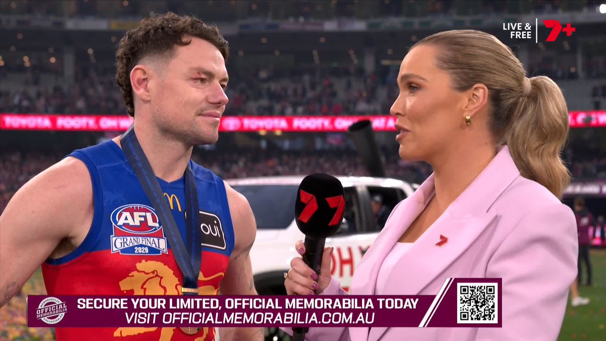 A female reporter in a pink blazer interviews a bloody AFL Grand Final 2026 player on the field for Channel 7.