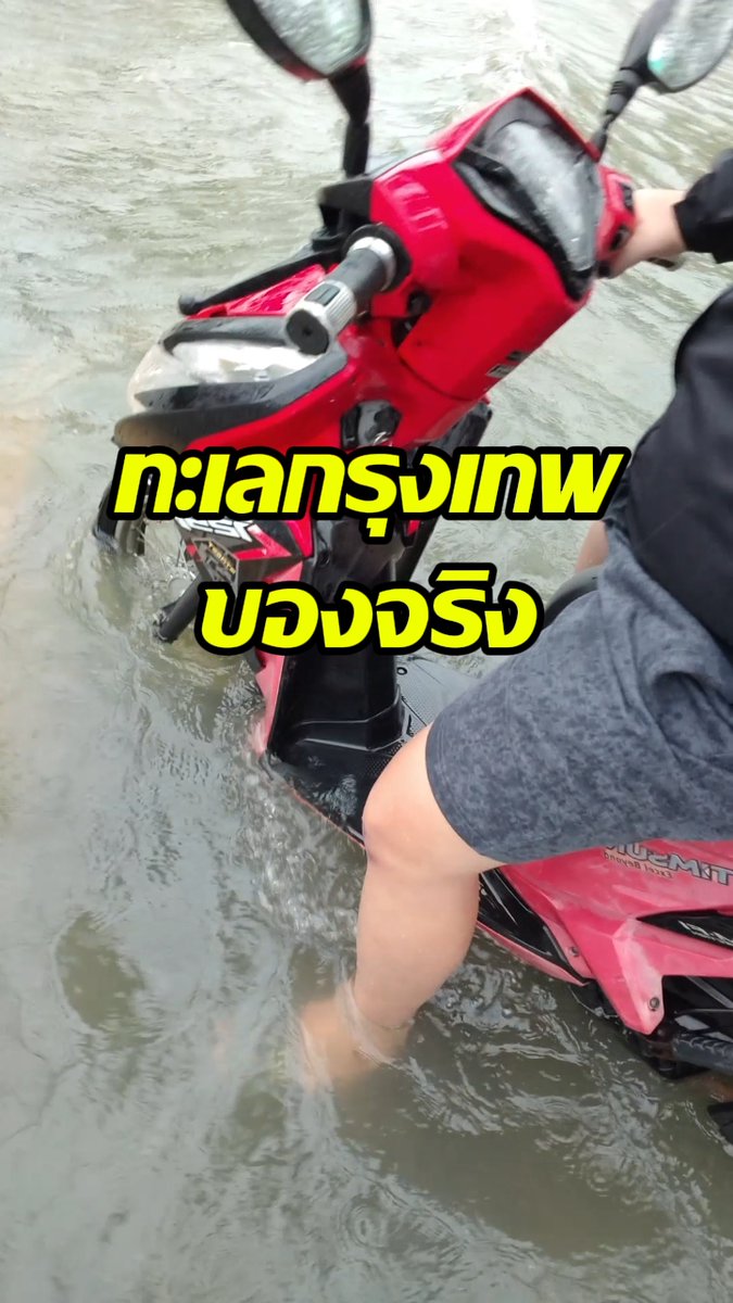 A person's leg is submerged in murky floodwater next to a red and black motorcycle, with overlaid Thai text reading 'ทะเลทรุดเทพ ของจริง' (Real sea/road collapse).