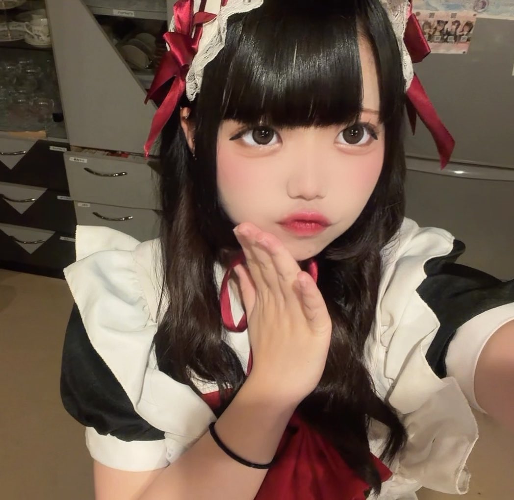 A close-up selfie shows a person in a classic black and white maid outfit with red bows, posing with their hand near their face.
