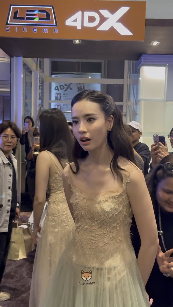 A woman in an elegant cream-colored floral dress attending an event at 'LED CINEMA 4DX', with 'foxycrush77' watermarked on the image.