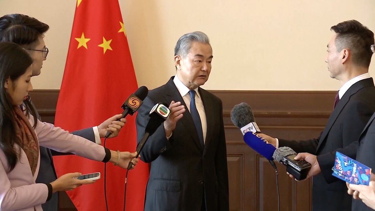 Chinese Foreign Minister Wang Yi speaks to the press in front of a Chinese flag, with microphones from various media outlets including CCTV. This image visually supports the news about President Xi Jinping's state visit and its impact on China-US relations.