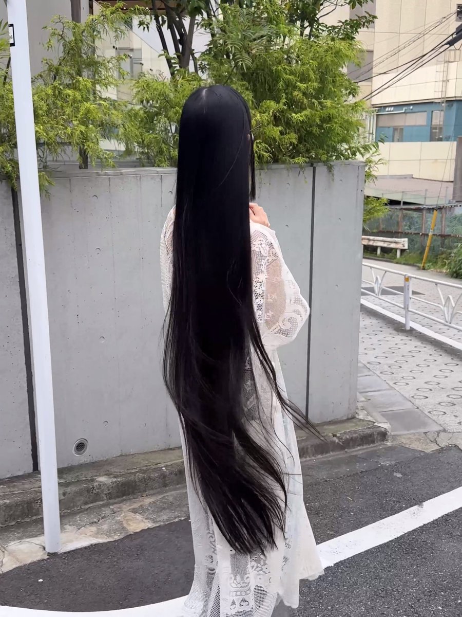 The image shows a person with extremely long, flowing black hair wearing a white lace dress, standing on a street from behind—giving them a ghostly, ethereal appearance. The caption connects to the post's joke about not having seen a ghost, as the figure's dark, cascading hair and pale clothing could easily be mistaken for a wandering spirit on the Japanese street.