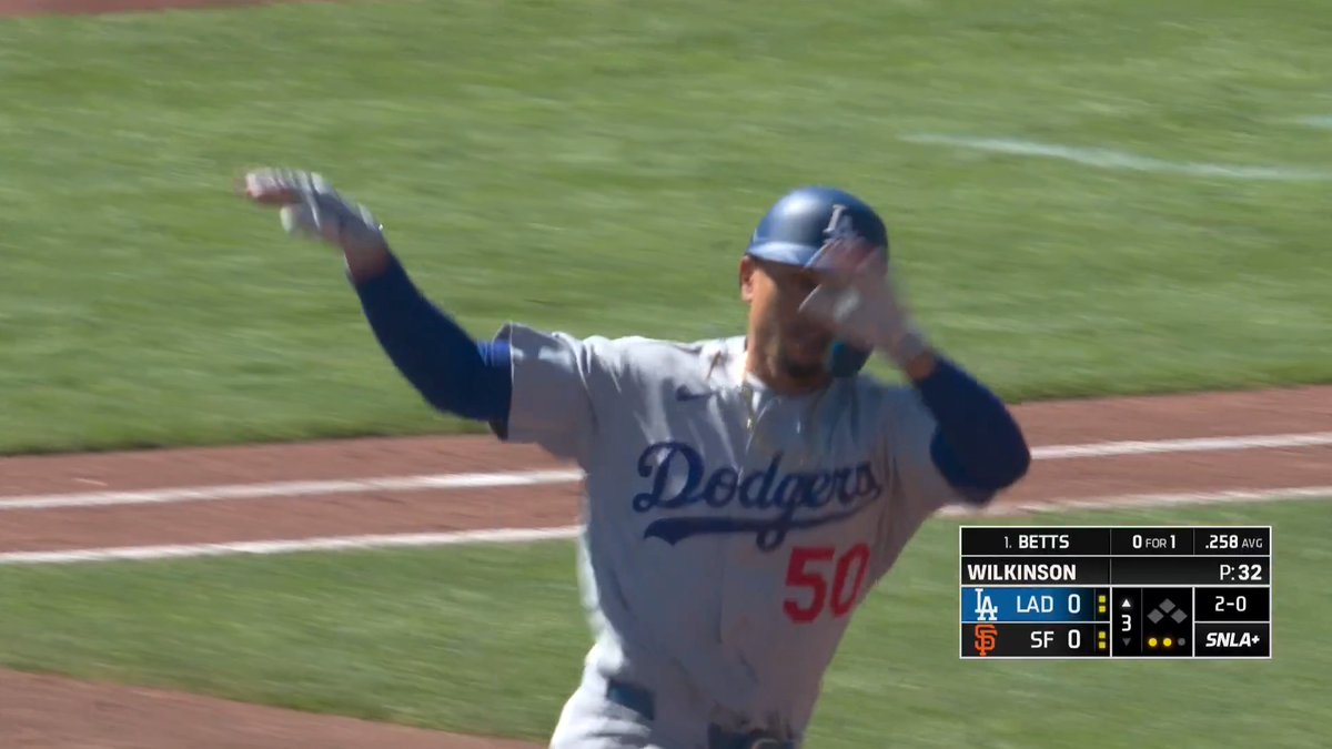 Dodgers player #50, Mookie Betts, celebrates triumphantly with his arms raised after what appears to be a home run, as shown on the SNLA+ scoreboard where he is listed as "1. BETTS" going 0-for-1 against the Giants' Wilkinson in a tied 0-0 game in the top of the 3rd inning. His emphatic celebration perfectly embodies the post's message that "Mookie showed no mercy!" as he unleashes an intense, almost fierce expression following his successful at-bat.