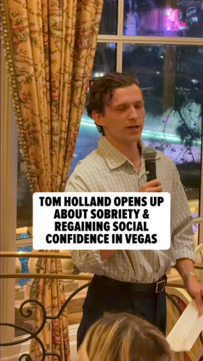 Tom Holland, holding a microphone, speaks at an event in Las Vegas while text overlay reads "TOM HOLLAND OPENS UP ABOUT SOBRIETY & REGAINING SOCIAL CONFIDENCE IN VEGAS," aligning with the post about him discussing his sobriety journey in Vegas.