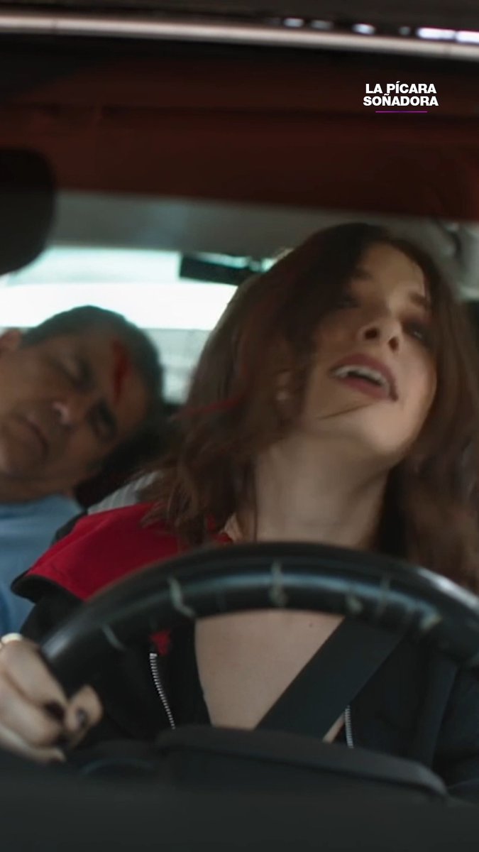 A woman with reddish-brown hair is driving a car while speaking, with a man visible behind her, accompanying the text "LA PÍCARA SOÑADORA" displayed in the corner—matching the hashtag for the show referencing the hostage and accident plotline.