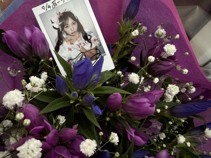 A bouquet of purple and white flowers contains a polaroid-style photo card with handwritten text in an Asian script.