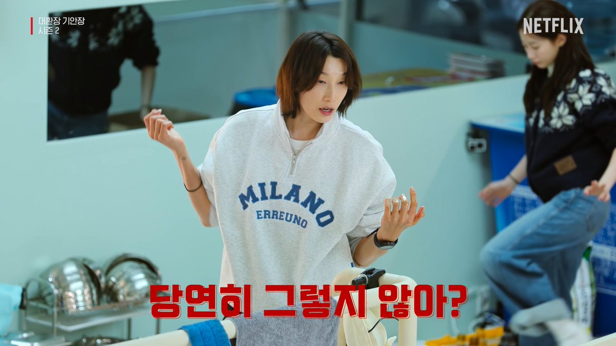 A woman with short hair wearing a gray "MILANO ERREUNO" sweatshirt gestures with a concerned expression in what appears to be a kitchen setting, while red Korean text reads "탕연희 그렇게 앉아?" (Are you sitting like that, Tang Yeon-hee?). The Netflix "대벌장 기안장 시즌 2" (Daewhanjang Gianjang Season 2) logo appears in the corner, promoting the show's new season featuring volleyball legend Kim Yeon-koung.