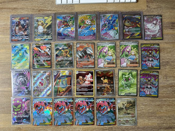 A collection of Pokémon trading cards arranged in rows on a wooden surface, including various holographic and rare cards.