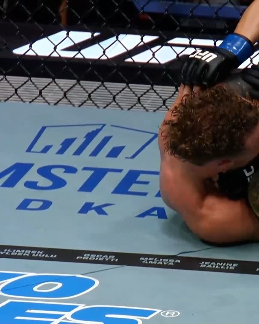 A UFC fighter with curly hair and a UFC glove on appears to be in a dominant position on top of an opponent on the mat during a fight.