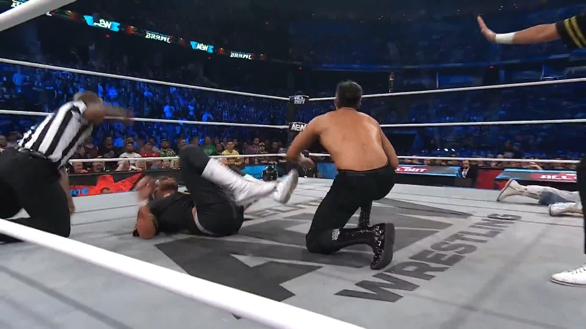 A professional wrestling match in an AEW ring shows a wrestler in a referee-style striped shirt knocking down an opponent while another wrestler kneels nearby, with "AEW" and "TNT" logos visible around the arena, capturing the action from the #AEWTailgateBrawl event where the Bang Bang Gang emerged victorious.