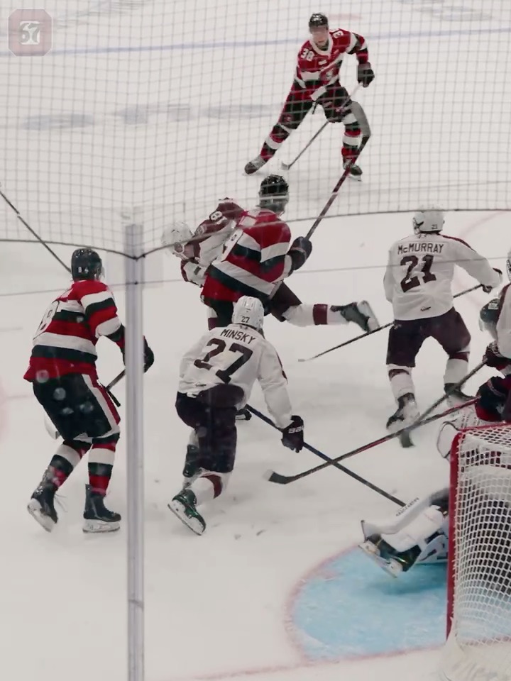 Hockey players in white jerseys (including one with 'MINSKY 27' and another with 'MURRAY 21') compete against players in red and black jerseys on the ice.