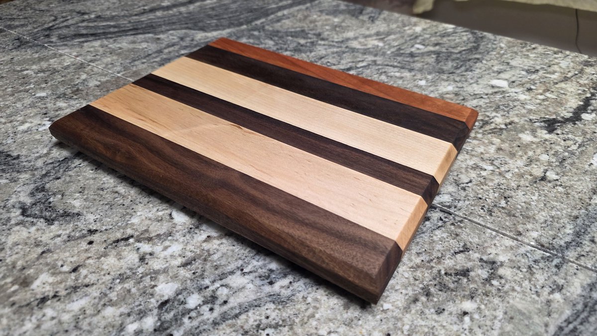 GDWorkbench's tweet photo. A low-angle look at this finished walnut, maple, and cherry face-grain prep/cutting board, showing the beveled edges and raised profile. Project GD-P-446: https://t.co/e38t15NAwH #GDWorkbench #CuttingBoard https://t.co/LxYljI8Nro