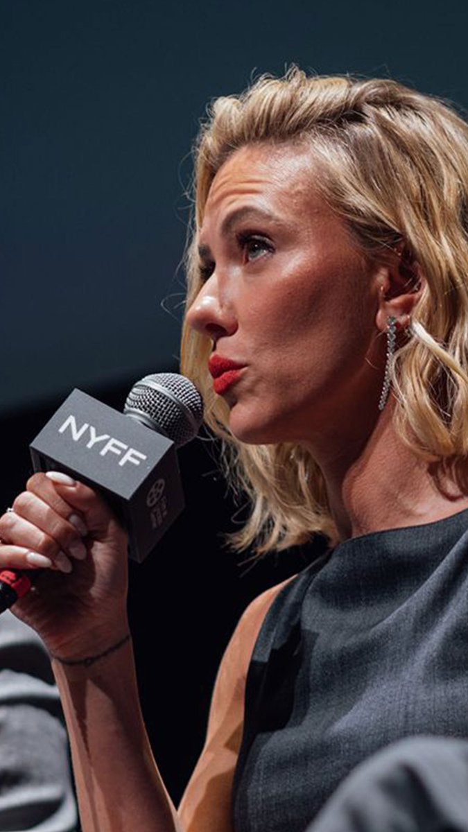 A blonde woman with red lipstick speaks into a microphone branded "NYFF," likely at a New York Film Festival event, with the commentator complimenting her appearance.