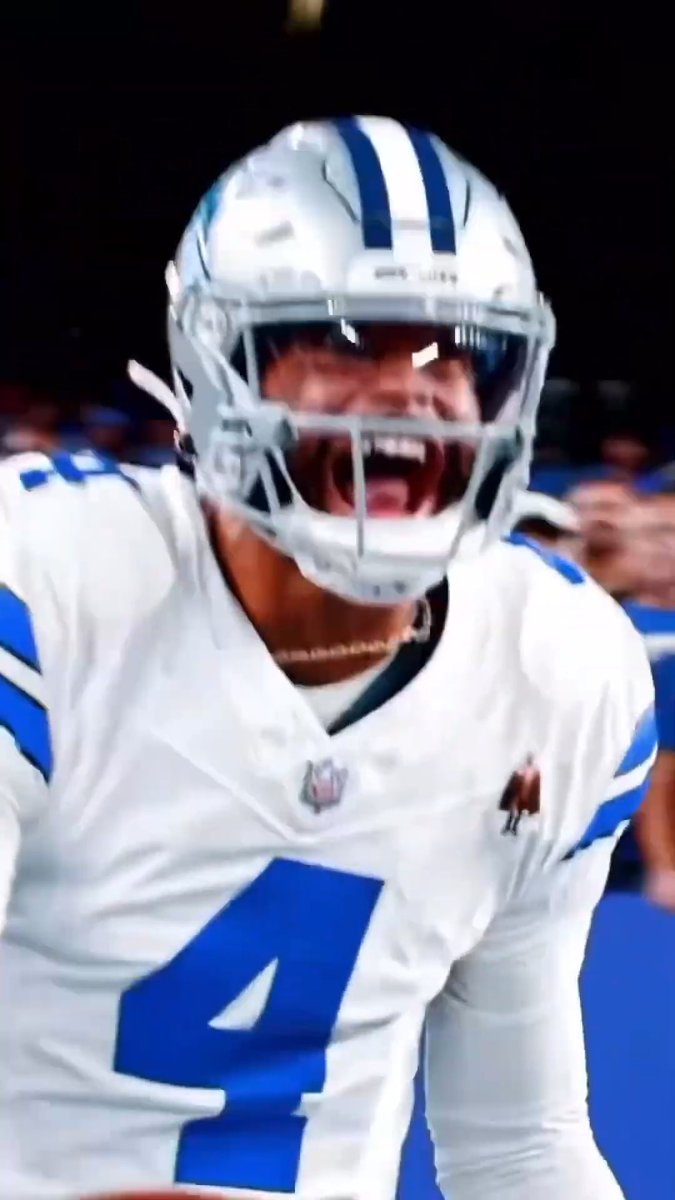 A Dallas Cowboys football player wearing a white and blue jersey with the number 4, shouting intensely from the sidelines.