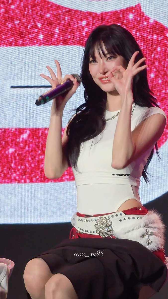 A female performer with long dark hair smiles and makes hand gestures while holding a microphone on stage in a white top and studded belt. Watermark reads 'ccccc_xu95'.