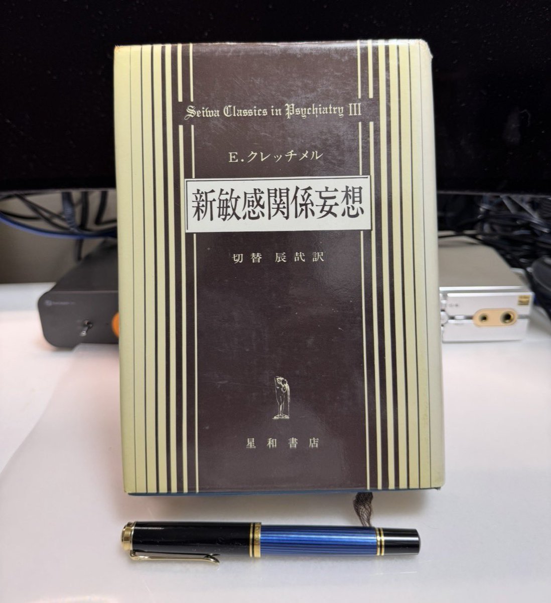 hidekisujita's tweet photo. 妄想を、その人の人生から
理解する

――クレッチメル著ーー

『新敏感関係妄想』

誰かが笑ったとき

「自分のことを笑っているの
ではないか」

と気になることはある。

たいていは一時の思い過ご
しとして消えていく。

ところが、その疑いが強まり、
周囲の何気ない会話や視線ま
でが自分への非難を意味する、
と確信されるようになったら
何が起きているのか。

精神科医
エルンスト・クレッチメル著

『新敏感関係妄想』

切替辰哉訳、星和書店刊

ドイツ語原著

『Der sensitive 
Beziehungswahn』

初版は1918年に刊行

は、この問いを、症状だけでな
くその人の性格、経験、置かれ
た環境から考えようとした本で
ある。

著者のクレッチメル

（1888–1964）

はドイツの精神科医である。

哲学や文学などを学んだ後に医
学へ進み、テュービンゲンでロ
ーベルト・ガウプのもと精神医
学を修めた。

本書は第一次世界大戦期の勤務
を経て完成した研究で、その後
クレッチメルはマールブルク、
さらにテュービンゲンで教授
を務めた。

1921年には、体格と気質の関
係を論じた『体格と性格』も発
表している。

ただし、この後年の体格論と
『敏感関係妄想』の臨床的な洞
察を、同じ評価で一括りにす
るべきではない。

本書が生まれた背景には

「パラノイア」

すなわち体系だった妄想をどう
捉えるかという当時の論争があ
った。

病気を症状の種類や経過から分
類することは重要である。

しかし、分類だけでは、なぜこ
の人が、この時期に、この内容
の妄想を抱くようになったのか
という問いに十分答えられない。

クレッチメルはそこへ目を向け
た。

彼が描いた「敏感」な人は、単
に傷つきやすい人ではない。

良心的で、恥や失敗を深く受け
止め、他人の評価を気にかける
人である。

そうした人が、本人にとって重
大な対人関係上の葛藤を抱え、
孤立した状況に置かれる。

すると、心の中で消化しきれな
い苦痛が

「周囲も自分の秘密を知り、非難
している」という確信

へ発展することがある

――これがクレッチメルの描い
た筋道だった。

ここでいう「関係妄想」とは、
本来は自分と無関係な出来事を、
自分に向けられた意味のある合
図として受け取ることである。

この本の衝撃は、妄想を奇妙な
発言の集まりとして眺めるだけ
でなく、本人にとって切実な意
味を持つ体験として読もうとし
た点にある。

クレッチメルは性格、出来事、
社会的状況の結びつきに注目
し精神症状が生じる過程をた
どった。

これは、患者の生活史を丁寧
に聴く精神病理学に長く影響
した。

刊行後には批判も受けパラノ
イアをめぐる彼の結論を、同
時代の大きな権威であったク
レペリンも受け入れなかった。

一方で、1920年代の書評は、
この著作の影響が広がってい
るとも記している。

後世から見ると、本書の価値
と限界は表裏一体である。

現在の主要な診断分類に

「敏感関係妄想」

がそのまま独立した病名として
定着しているわけではない。

同じような訴えの背景にも、気
分の障害を含むさまざまな状態
があり得る。

性格と苦しい経験が重なれば必
ず妄想が生じる、という単純な
因果関係として扱うことはでき
ない。

また、原著の症例を分ける言葉
には当時の性や社会的立場に関
する価値観が色濃く表れている。

本人の苦痛を理解しようとする
視点を、本人の

「性格のせい」

にする説明へ転じてしまう危険
にも注意が必要だ。

それでも、この古典が読み継が
れる理由は明瞭である。

診断名を知ることと、目の前の
人に何が起きたのかを理解する
ことは、同じ作業ではない。

クレッチメルは後者の問いを精
神医学の中心に据えた。

『新敏感関係妄想』

は、今日その理論を無批判に採
用するための本ではなく、症状
を持つ人の人生を診断の陰に隠
さないために読む本なのである。