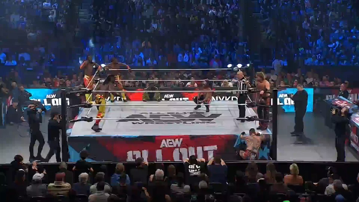 A wrestling match taking place in an AEW (All Elite Wrestling) ring surrounded by a large, cheering crowd in an arena.