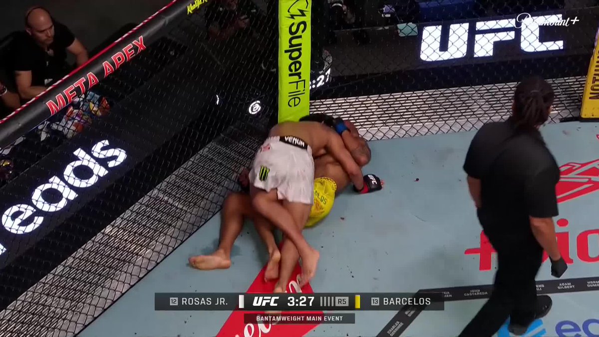 A UFC bantamweight main event between #12 Rosas Jr. and #14 Barcelos, with 3:27 remaining in round 5, showing the fighters grappling against the cage near Meta Adex and Easygo advertisements.