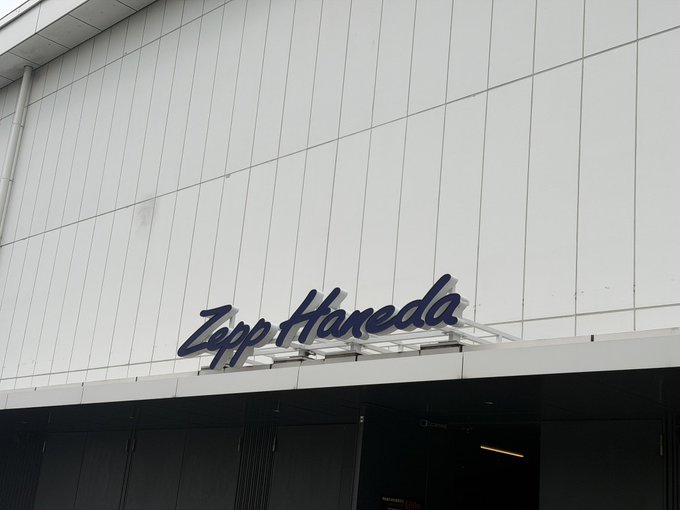 A white building exterior displays a dark blue cursive sign reading 'Zepp Haneda'.