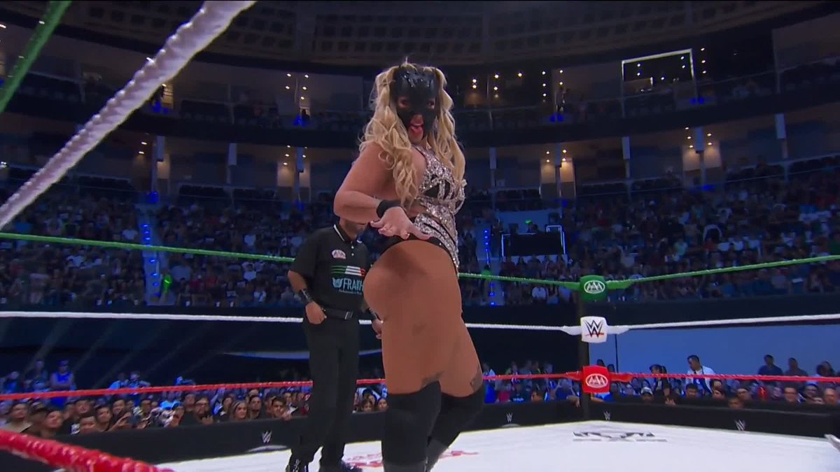 A masked blonde wrestler in a sparkly outfit stands in a wrestling ring with a referee behind her, as a packed arena crowd watches on, with "#AAAenFOX" and "KIA" logos visible on the turnbuckles—capturing the ongoing competitive spirit of the lucha libre event highlighted in the post.