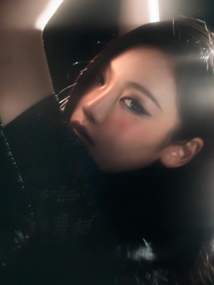 A stylized, cinematic portrait of a woman with dramatic eye makeup, tilted on her side in dark, moody lighting.