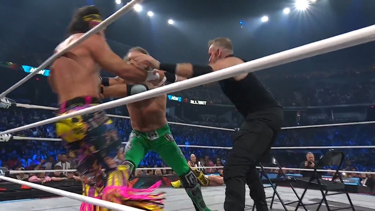 Three wrestlers are engaged in a match inside a wrestling ring, with a sign reading 'H.L.N. BAIT' visible in the background.