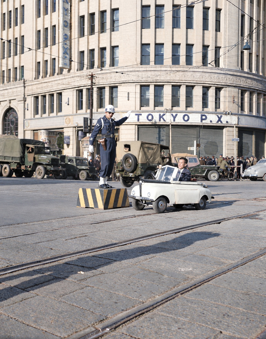 old_nippon's tweet photo. 1947年（昭和22年）12月に銀座四丁目交差点を走るミニ電気自動車と、交通整理をする進駐軍MP。背景にある建物は、当時アメリカ軍の売店「TOKYO P.X.」として接収されていた服部時計店（現在の銀座・和光）です。※彩色写真 https://t.co/PmP9LAto3D